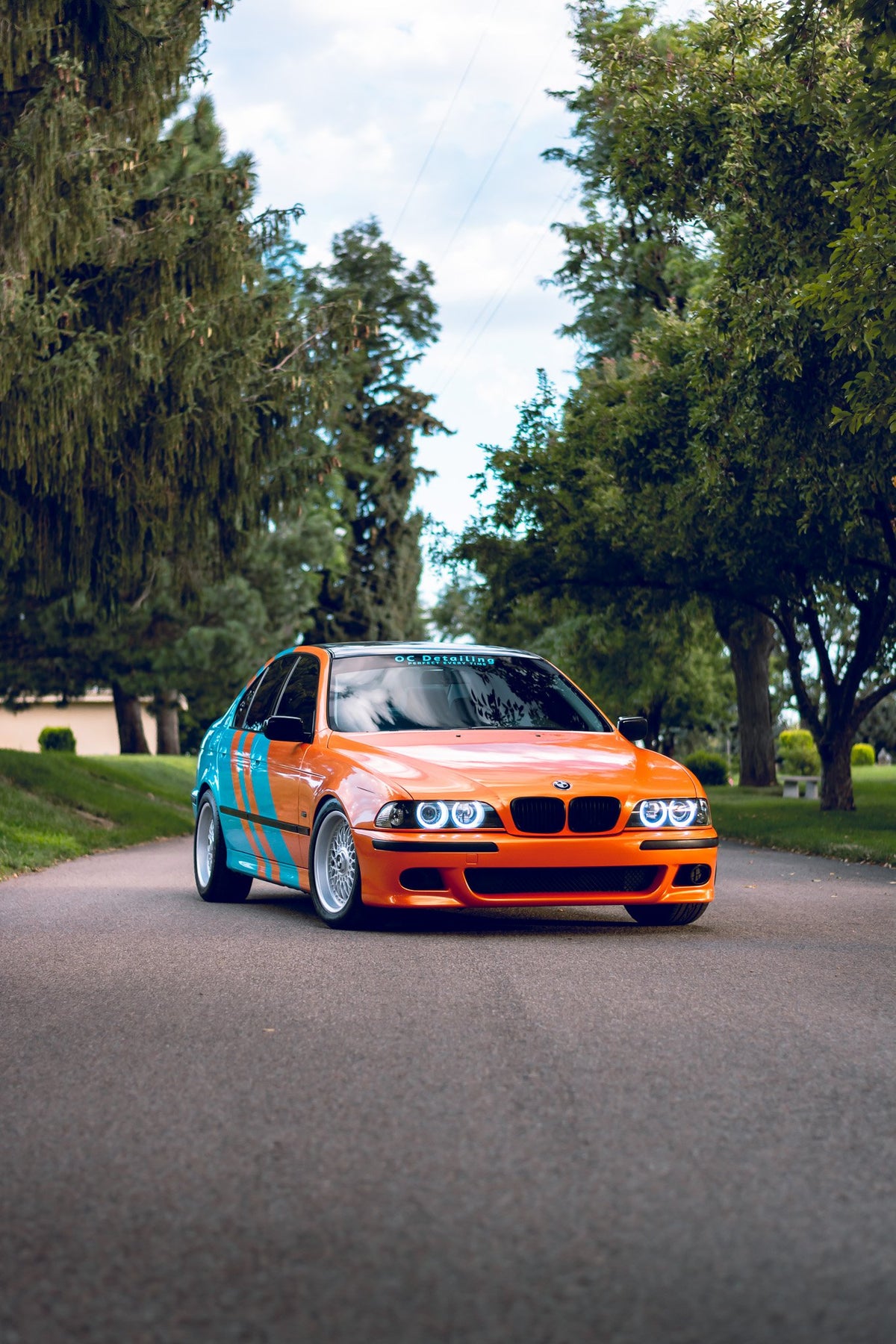 older bmw wrapped in blue and orange parked in middle of roadway